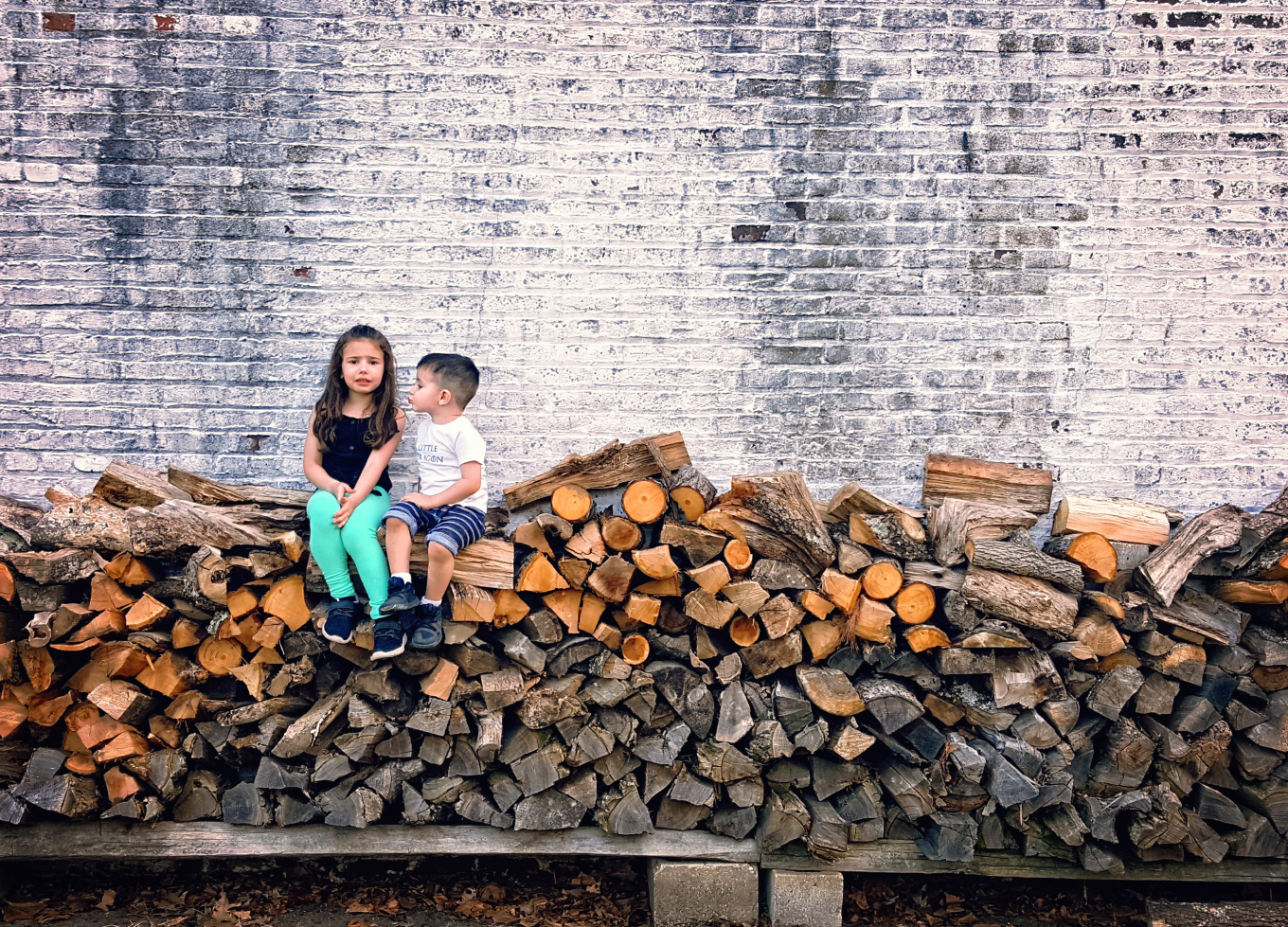girl and boy sitting on stacked logs