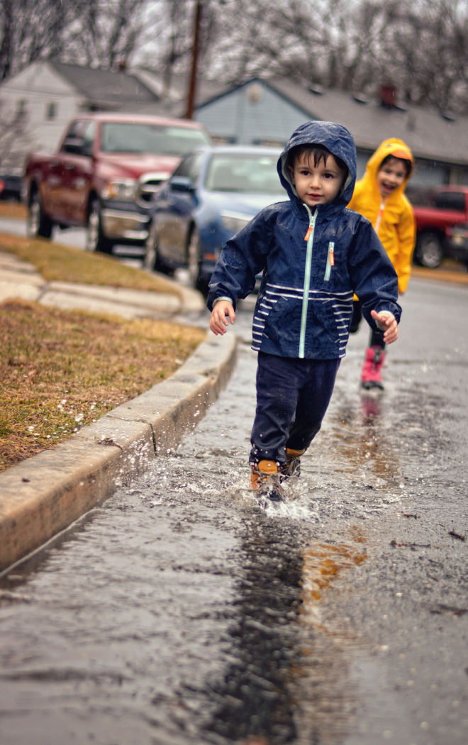 girl and boy wearing raincoats walking in rain