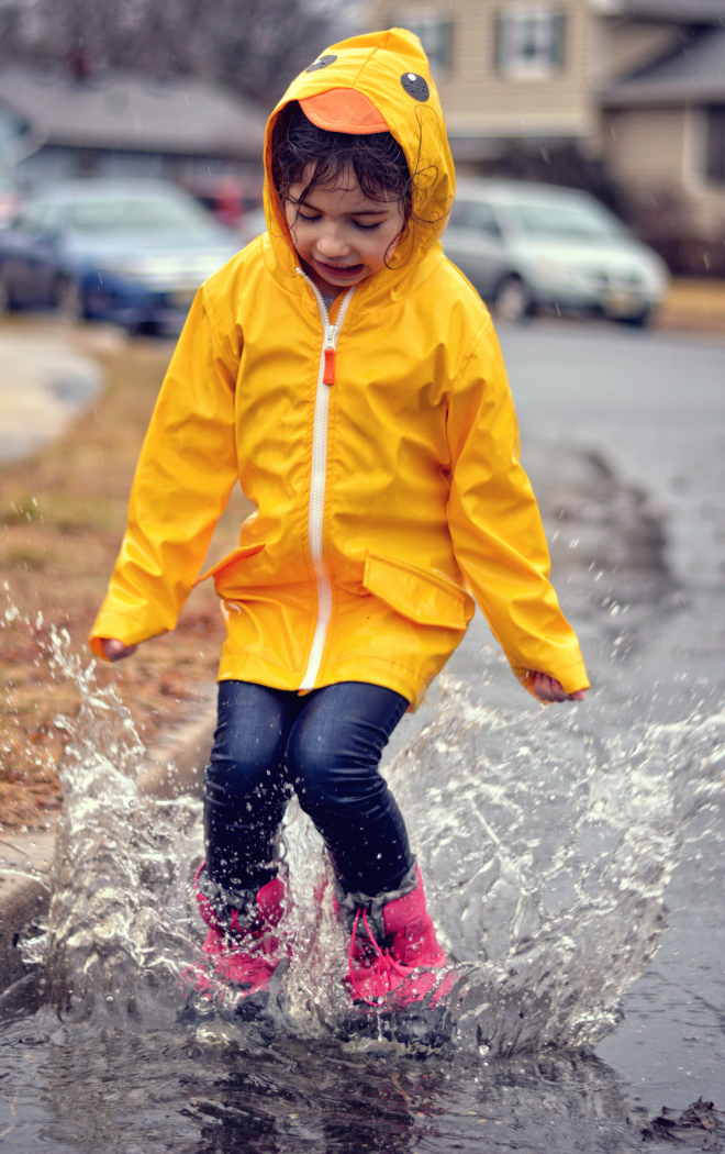 girl in raincoat jumping in puddle